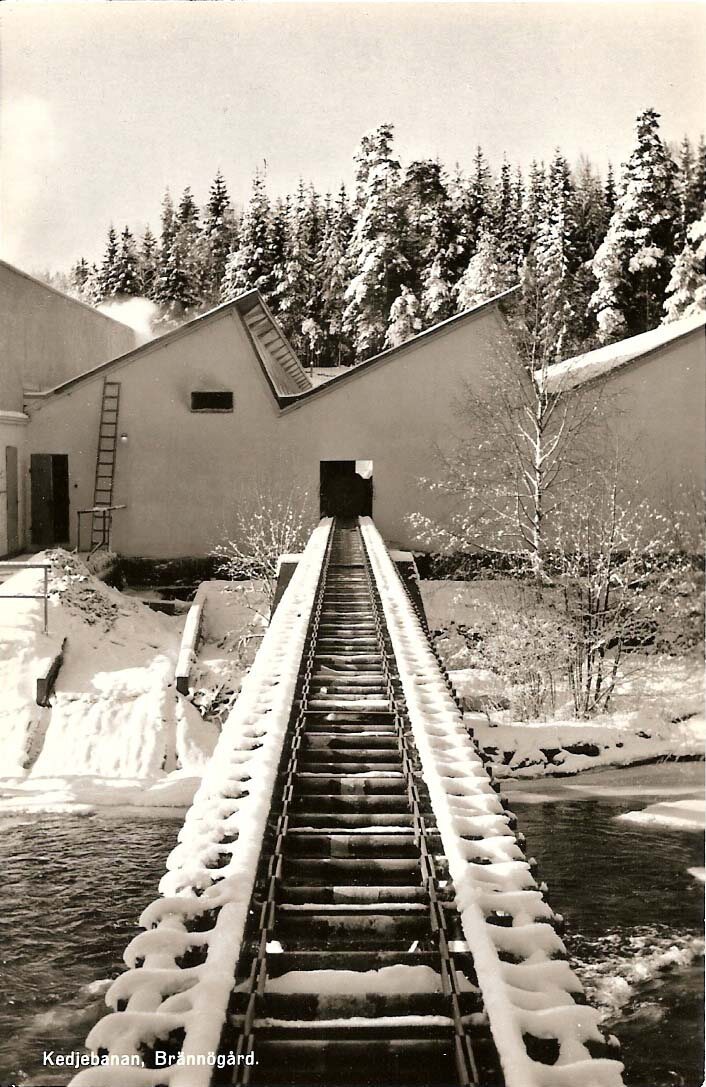 Snötäckt kedjebana som leder över vatten till en industribyggnad vid Brännögård