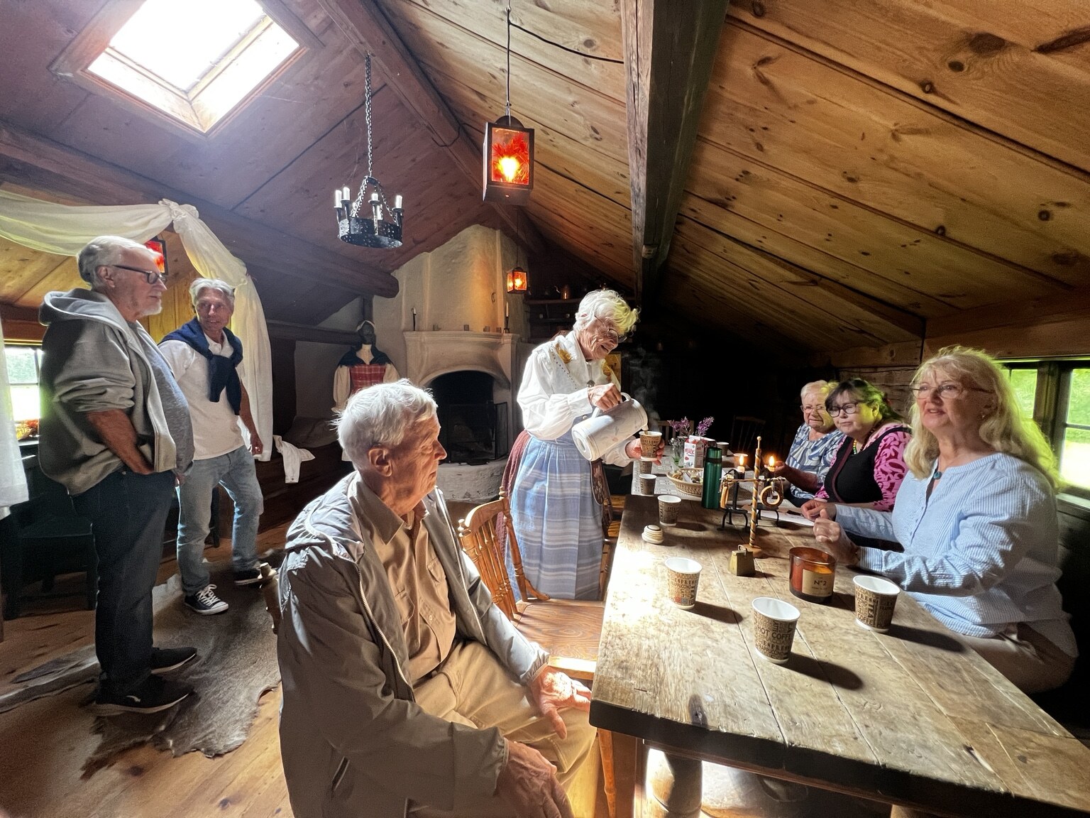 Besökare runt ett långbord medan kaffe serveras inne i Ryggåsstugan